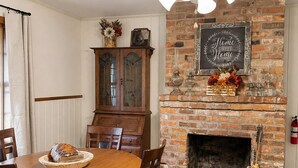 Zona pranzo con camino in mattoni, tavolo di legno, sedie e ventola a soffitto.