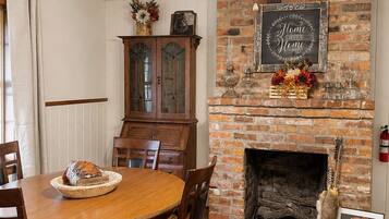 Comedor con chimenea de ladrillo, mesa de madera, sillas y ventilador de techo.