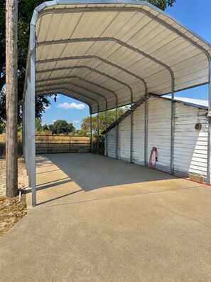 A covered outdoor area with a concrete floor, metal beams, and a white building in the background.