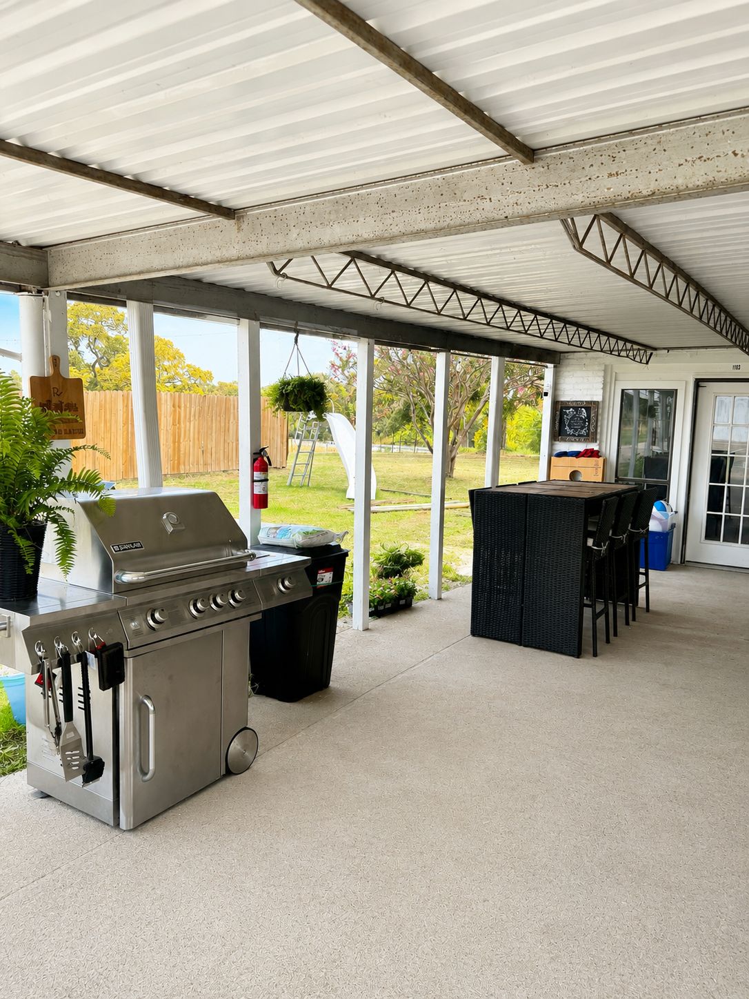 Een terras buiten met een roestvrijstalen barbecue, een bar en een overdekte zithoek.