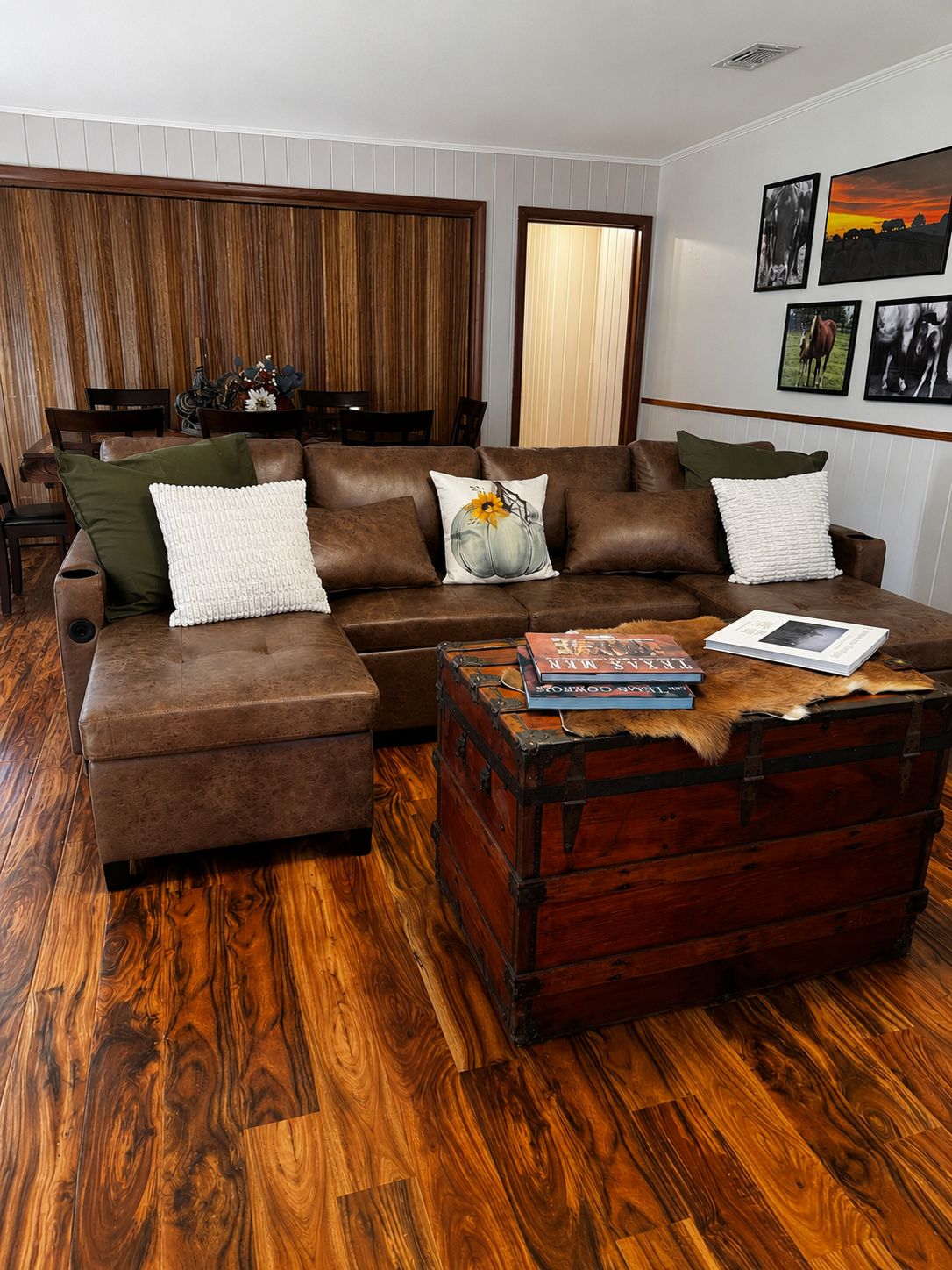 Un salon chaleureux avec un canapé en cuir marron, un pouf assorti et une table basse en bois rustique, sur laquelle sont posés des livres.