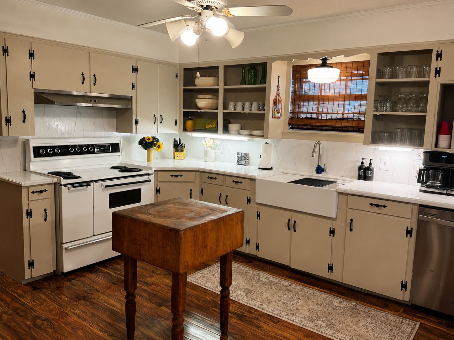 A kitchen with white cabinets, a stove, a sink, and a ceiling fan.
