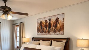 Una camera da letto con un letto grande, un ventilatore a soffitto, un quadro con dei cavalli, un comodino e una lampada.