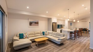 A modern living room with a sectional sofa, a wooden coffee table, and a dining area with a large table and chairs. - Bay Lookout @ Cape Villas (Dunsborough)