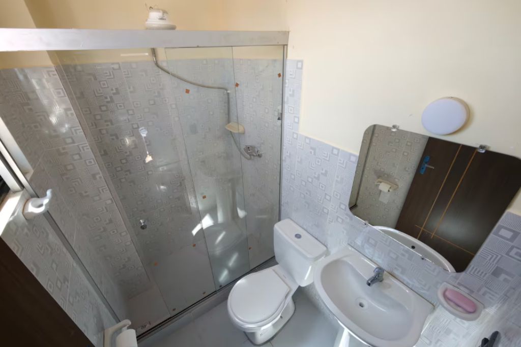 Un baño con ducha de vidrio, inodoro blanco y lavamanos con espejo.