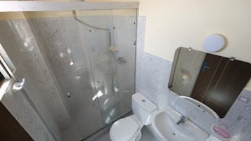 Un baño con ducha de vidrio, inodoro blanco y lavamanos con espejo.