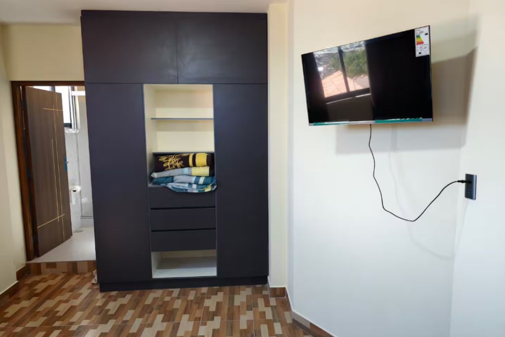 A room with a wardrobe, a flat-screen TV mounted on the wall, and a patterned floor.