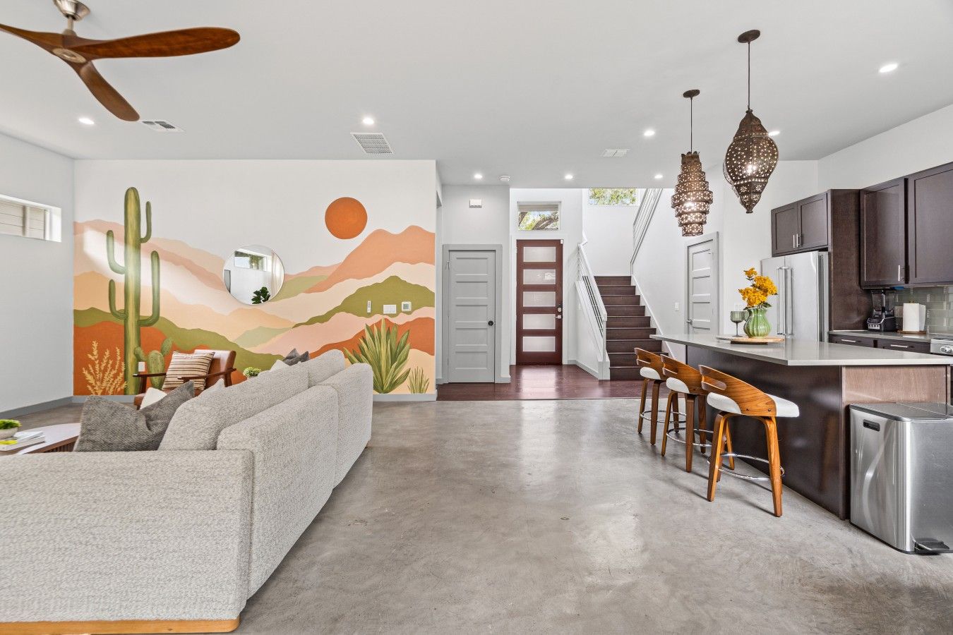 A modern kitchen with a bar area, a dining space with a sofa, and a living room with a large mural.