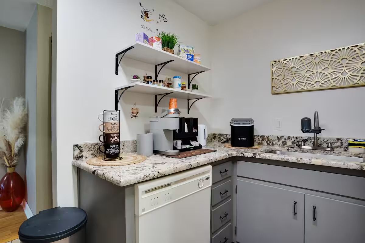 Una cocina con cafetera, estantes con diversos objetos y un adorno en la pared.