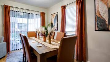 Uma sala de jantar com uma mesa de madeira, cadeiras e um vaso com plantas secas.