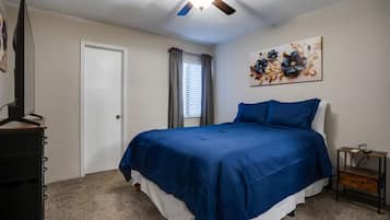 A bedroom with a bed, a ceiling fan, a door, a window with curtains, and a wall-mounted artwork.