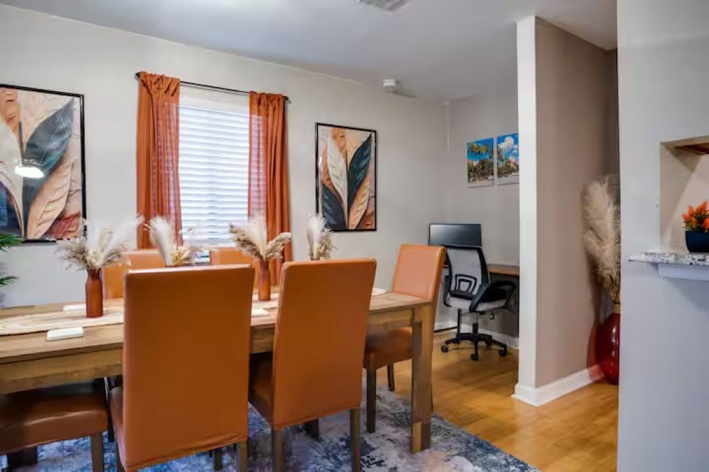 Uma sala de jantar com mesa de madeira, cadeiras laranjas e tapete azul.