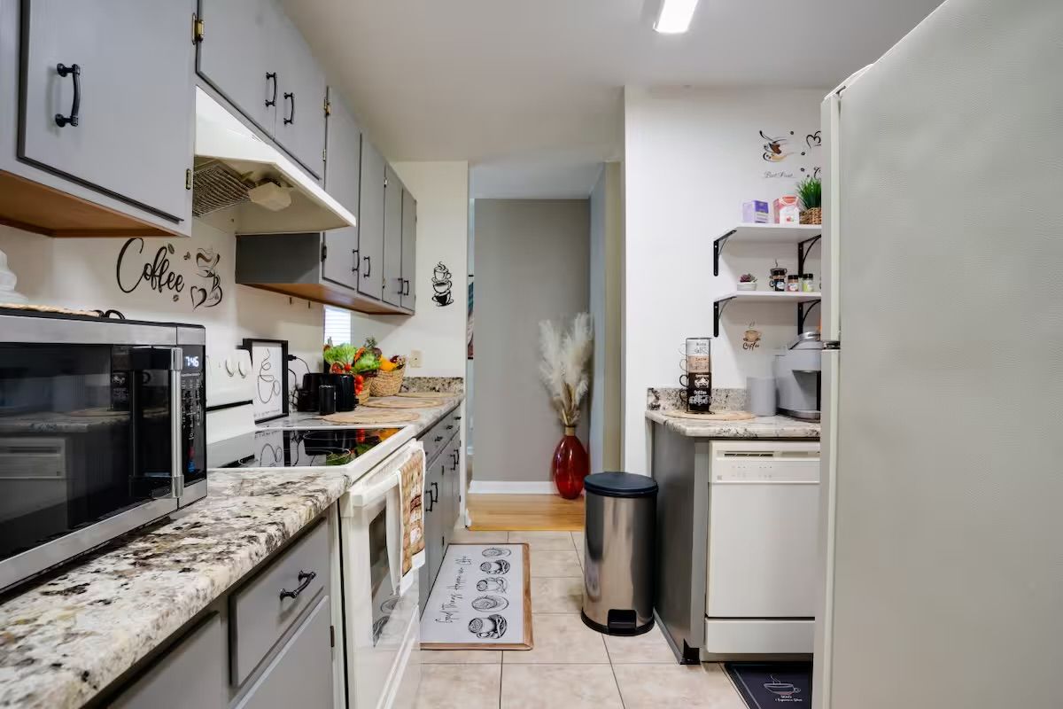 Cozinha compacta com micro-ondas, fogão e armários. Há uma lixeira e uma geladeira pequena.