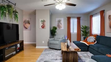 A living room with a flat-screen TV, a ceiling fan, a sofa, a coffee table, and a grey armchair.