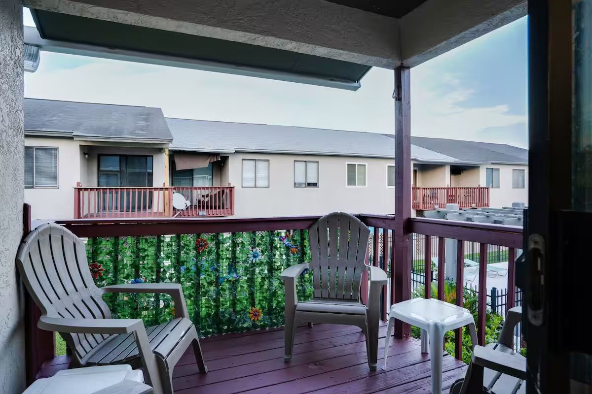 A balcony with two Adirondack chairs and a small table, overlooking a residential area with multiple houses.