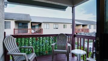A balcony with two Adirondack chairs and a small table, overlooking a residential area with multiple houses.