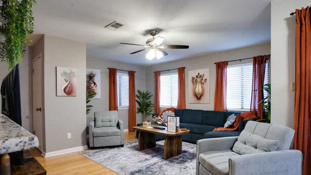 Ein Wohnzimmer mit Deckenventilator, einem grauen Sofa, einem Couchtisch und einem grauen Sessel.