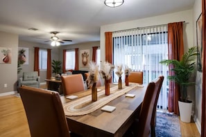 Uma sala de jantar com uma longa mesa de madeira, várias cadeiras e vasos decorativos.
