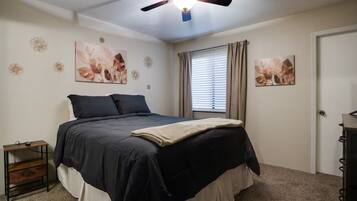 A bedroom with a bed, a ceiling fan, a window with curtains, and wall art.