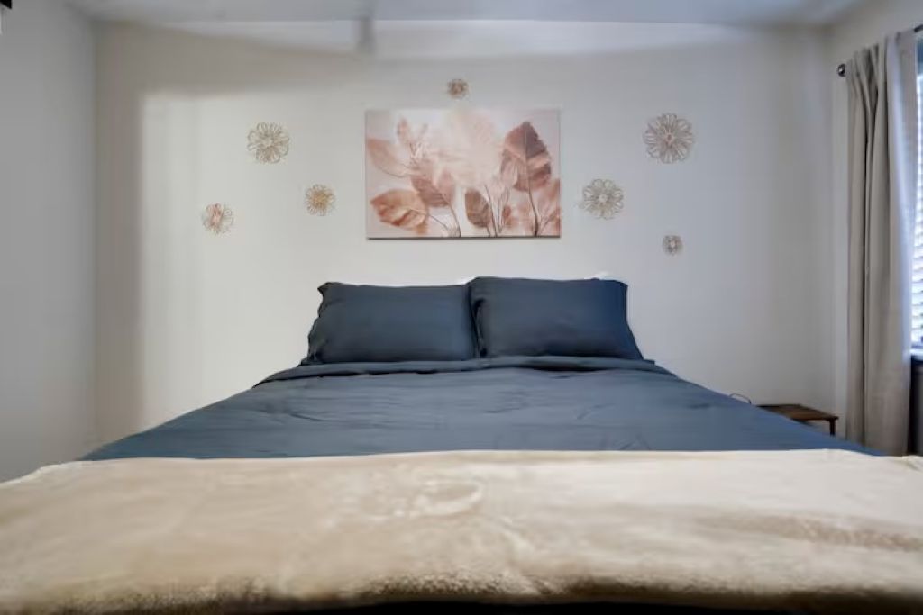 Um quarto com uma cama, uma obra de arte na parede e uma janela com cortinas.