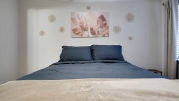 Um quarto com uma cama, uma obra de arte na parede e uma janela com cortinas.