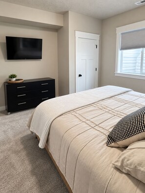 A bedroom with a bed, a dresser, a television, and a window with blinds.