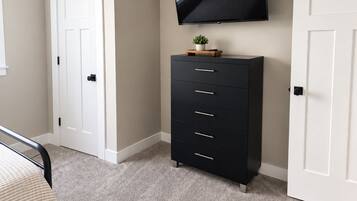 A bedroom with a bed, a dresser, a television mounted on the wall, and two doors.