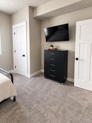 A bedroom with a bed, a dresser, a television mounted on the wall, and two doors.