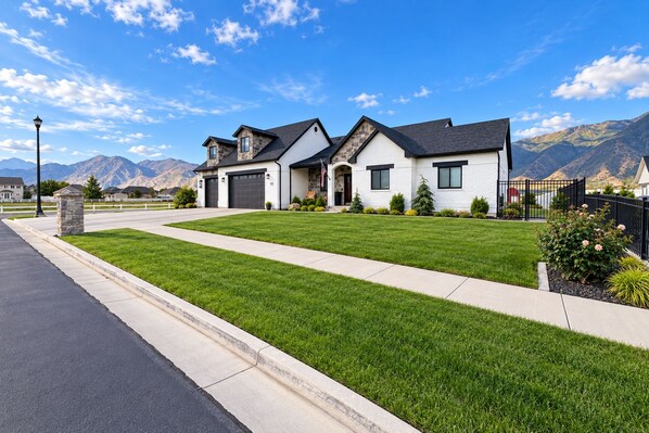 A two-story house with a well-maintained lawn, a driveway, and a mountain backdrop.