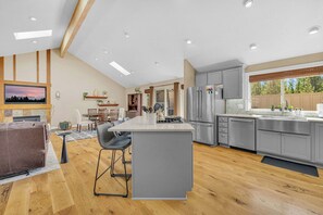 A modern kitchen with a large island, grey cabinetry, and a dining area with a fireplace. - AC, Luxury, Comfort, Family, Hot tub, Privacy (Sunriver)