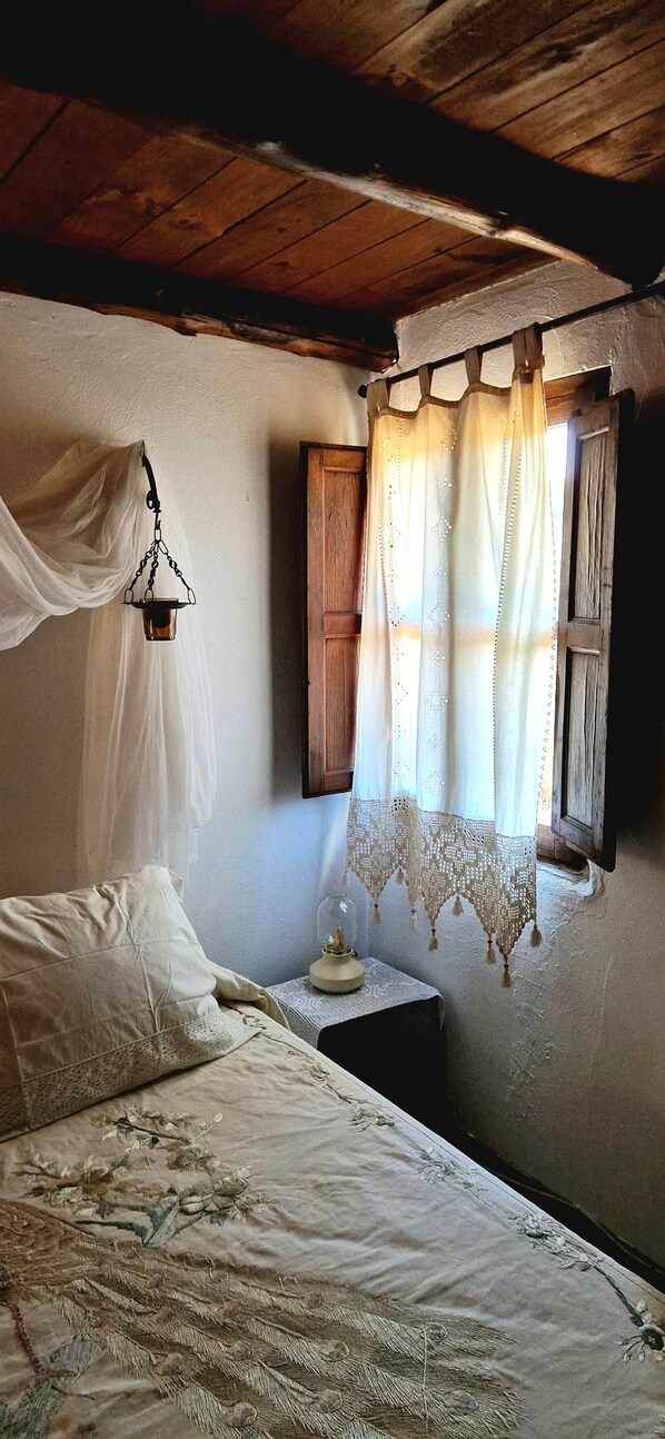 Une chambre avec un lit, un luminaire suspendu, une fenêtre avec des rideaux et une tête de lit en bois.