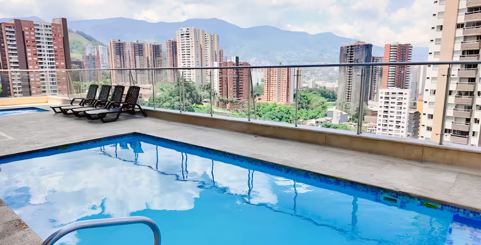 Piscina en la azotea con sillas de descanso y vistas de edificios altos circundantes.