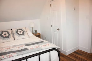 A bedroom with a bed, pillows, a nightstand, a lamp, and a door.