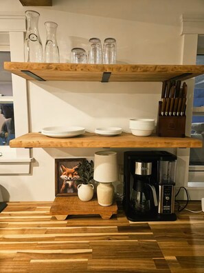 A kitchen with wooden shelves holding glassware, plates, and a coffee maker.