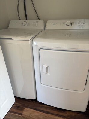 Two front-loading washing machines with control panels, a power cord, and a wooden floor.