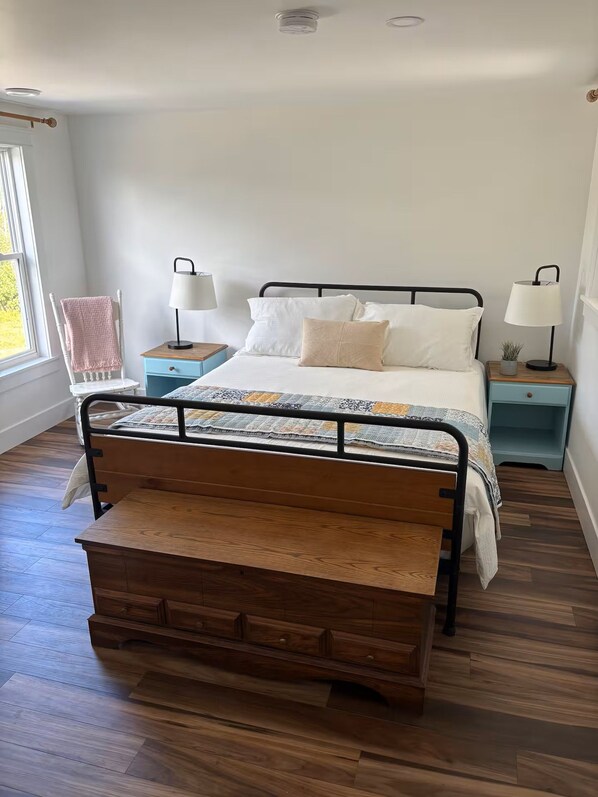 A bedroom with a wooden bed, two bedside tables, a window, and a view of the outdoors.