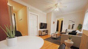 A modern living room with a round white table, a sofa, a television, and a ceiling fan. - Homey 1BR Space Apartment (Chicago)