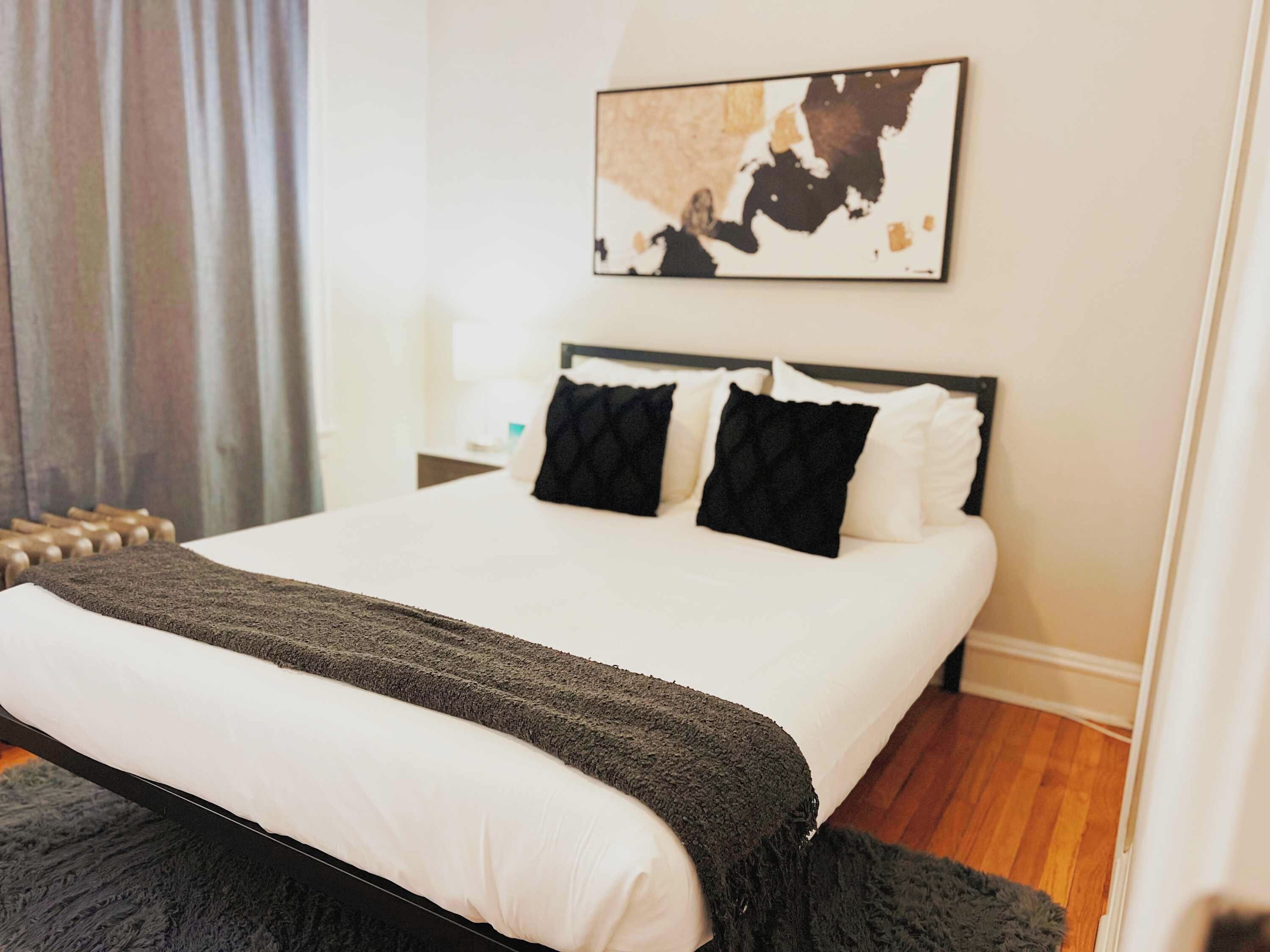 Una cama bien hecha con edredón blanco y gris oscuro, dos almohadas negras y una manta gris oscuro.