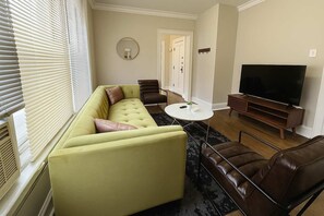 A living room with a sectional sofa, a coffee table, leather chairs, a TV, and a fireplace. - Nice 1BR Spot, Unwind & Relax (Chicago)