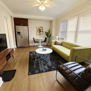 A living room with a yellow sofa, a black leather chair, a wooden coffee table, and a ceiling fan.