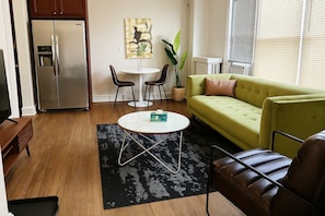 A modern living room with a green sofa, a coffee table, and a dining area with two chairs.