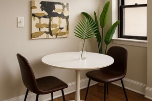 A round white table with two brown leather chairs, a glass vase with a plant, and a piece of abstract art on the wall. - Nice 1BR Spot, Unwind & Relax (Chicago)