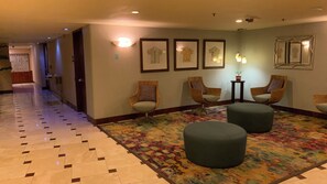 Un couloir doté d’un revêtement de sol à motifs, un espace détente avec des fauteuils et des poufs, et des tableaux encadrés accrochés aux murs.