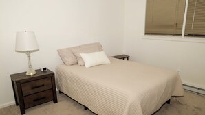 A bedroom with a bed, a nightstand, a lamp, and a window with blinds. - Tranquil 2-bedroom townhome with AC in charming Troy (Troy)