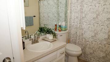 A bathroom with a sink, mirror, toilet, and shower curtain.