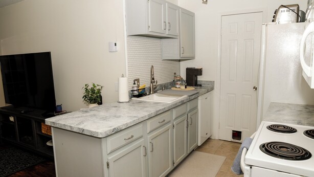 A kitchen with white cabinets, a stove, a sink, and a television. - Tranquil 2-bedroom townhome with AC in charming Troy (Troy)