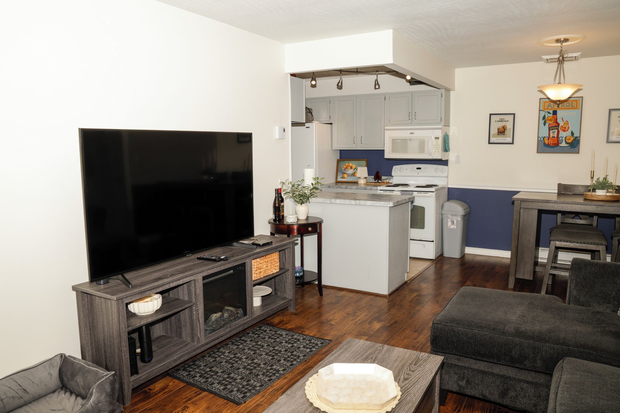 A modern living room with a flat-screen TV, a fireplace, and a dining area with a kitchen in the background.