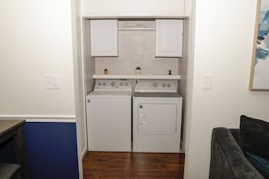 A compact laundry room with a washer and dryer, a small shelf with decorative items, and a painting on the wall.