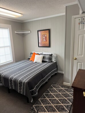 Quarto com cama, quadro na parede, porta e janela.