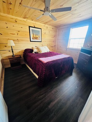 A bedroom with a bed, a ceiling fan, a nightstand, a dresser, and a window.